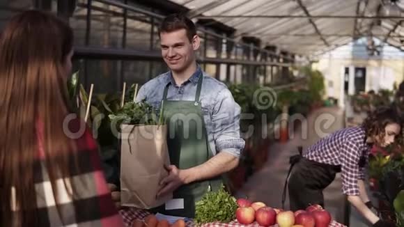 穿着绿色围裙的欧洲销售员的肖像将棕色纸袋中的有机食品送给女性顾客视频的预览图