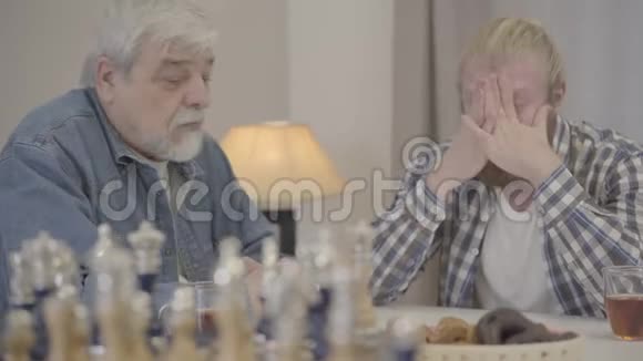 一个聪明的老人的特写镜头让成年儿子在家里平静下来老年男性退休人员与小胡子男谈话的肖像视频的预览图