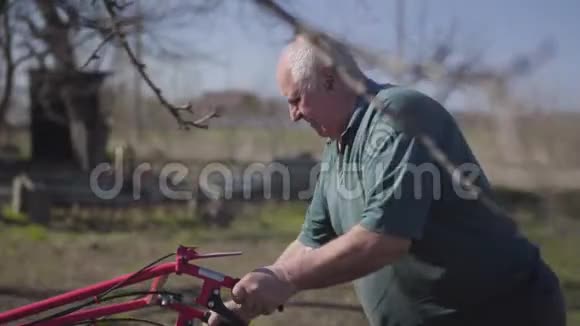 早春疲惫的老白种人犁地的肖像成熟的男性农民用犁沟器做沟视频的预览图