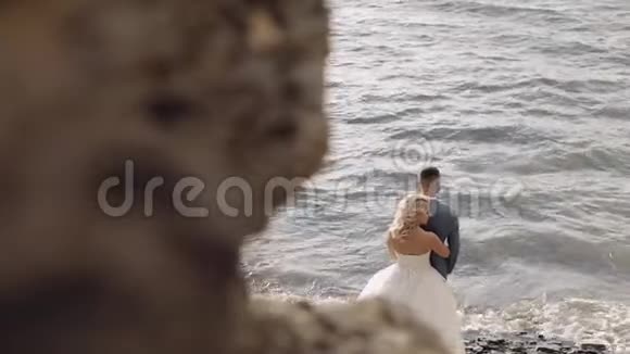 新婚夫妇站在河岸上新娘拥抱新郎新婚夫妇视频的预览图