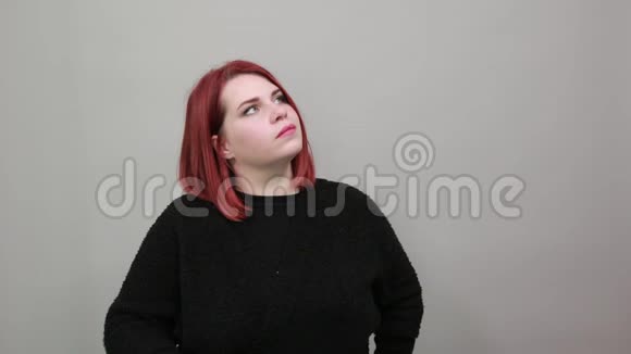 年轻的红头发胖女人穿黑色毛衣女人想用手摸下巴视频的预览图