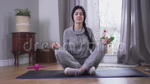 冷静的黑发白种人女人坐在瑜伽垫上闭着眼睛年轻女子在艰难的一天后平静下来生活方式视频的预览图
