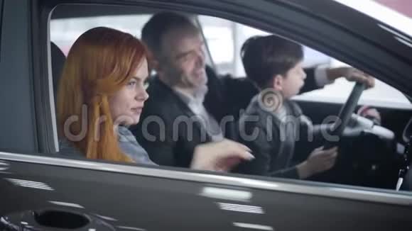 侧面观看美丽的红头白种人妇女坐在汽车沙龙与家人重点改变丈夫和儿子视频的预览图