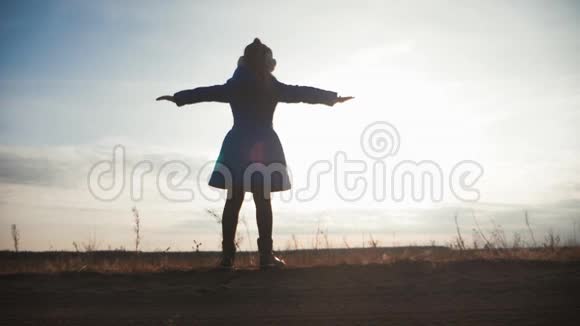 剪影女孩站在田野里在日落时张开双臂童年梦想的概念视频的预览图
