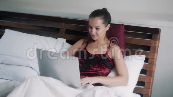 快乐的女孩在笔记本电脑上工作在床上喝橙汁视频的预览图