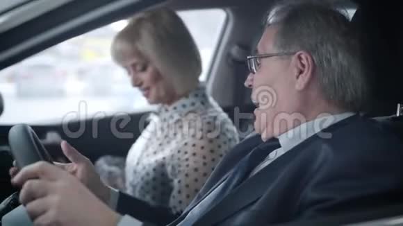 一位成功的老白种人商人和漂亮的妻子坐在汽车沙龙里给她钥匙视频的预览图