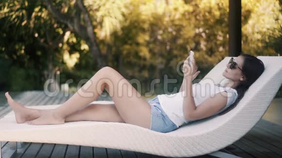 Tranquil女士使用智能手机躺在度假胜地的沙发上视频的预览图