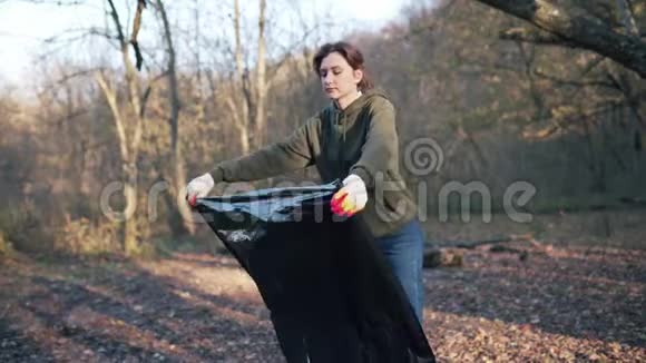一个准备在树林里收集垃圾的年轻学生打开一个黑色的大垃圾袋受污染的自然救助视频的预览图