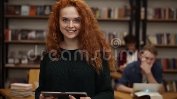 一位漂亮的长着红色头发的欧洲女学生站在高中图书馆的画像微笑着看着视频的预览图