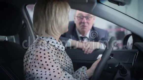 侧面观看美丽成熟的高加索女人坐在司机座位上与年迈的丈夫交谈快乐的金发女郎视频的预览图