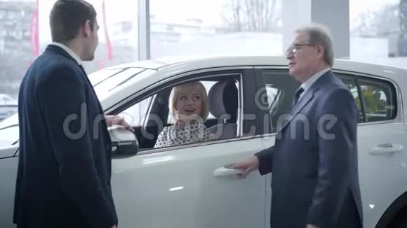 两个白种人男子站在新车旁边的经销商作为美丽的成熟女人坐在里面三个人视频的预览图