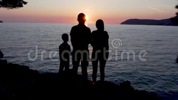 日落时站在海边的一个年轻家庭的剪影视频的预览图