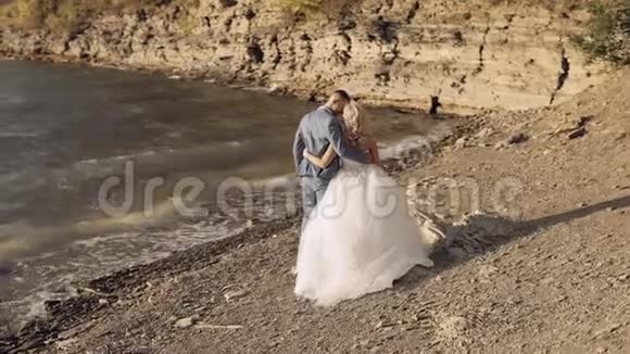 新婚夫妇在河岸上散步新娘拥抱新郎新婚夫妇视频的预览图