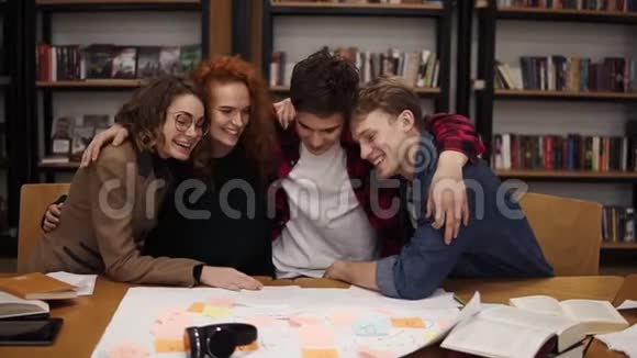 描绘了不同的朋友同学坐在大学图书馆的桌子上拥抱拥抱对方已经准备好了视频的预览图