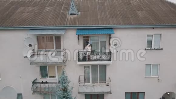 身着晚礼服的新娘站在她家的阳台上结婚的早晨空中景观视频的预览图