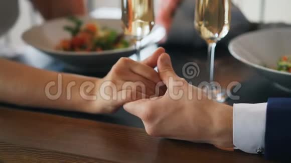 两只手的特写镜头男女放在桌上配着闪闪发光的香槟酒杯和带食物的盘子浪漫视频的预览图
