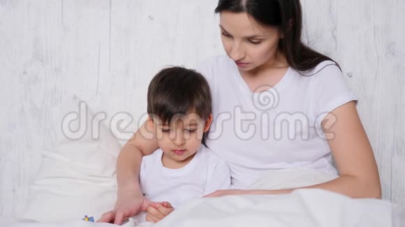 母亲和儿子坐在白色的床上拿着一辆木制的救护车视频的预览图