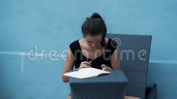 年轻女子坐在日光浴床上写日记使用移动蓝色背景视频的预览图