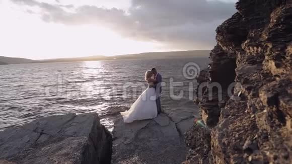 新婚夫妇在海边的山坡上日落新郎和新娘视频的预览图