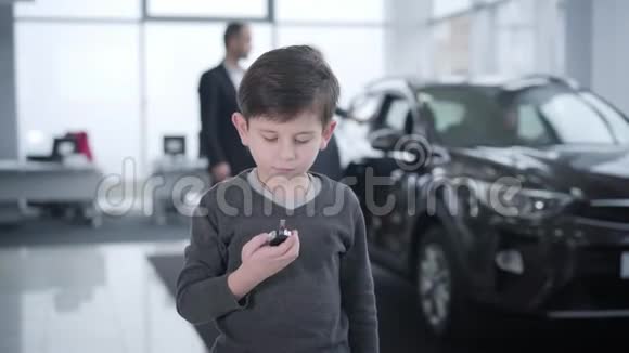 一幅快乐的小白种人男孩拿着车钥匙在展厅里跳跃的肖像站在车旁边的父母视频的预览图