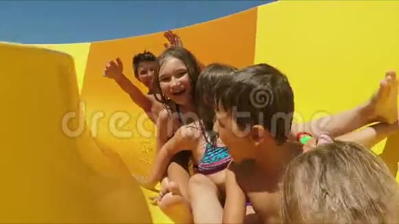 一群快乐的孩子正在水上公园里骑着黄色橙色的滑梯视频的预览图
