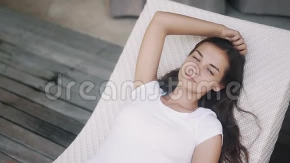 身穿白色t恤的女人躺在靠近游泳池的日光浴床上放松身心享受假期视频的预览图