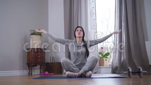 棕色皮肤的白人女人坐在瑜伽垫上举起双手把它们放在一起冥想视频的预览图