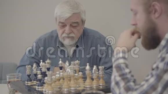 集中成熟的白人男子与成年儿子下棋的肖像有重点的老年退休人员有胡子休息视频的预览图