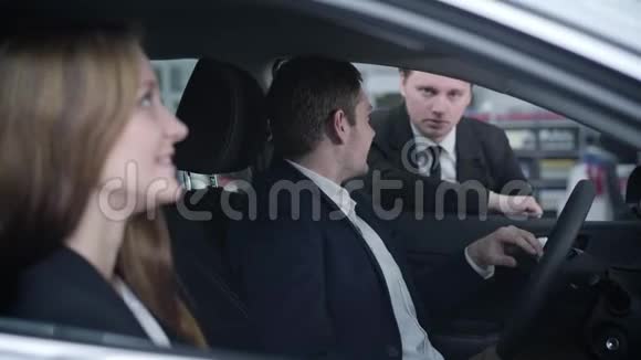 侧面观看英俊的年轻白种人男子坐在车上与妻子和经销商交谈微笑的男人和女人选择视频的预览图