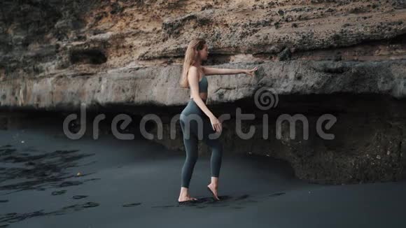 在悬崖附近的黑沙滩上做伸展运动的女人视频的预览图