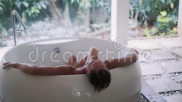 肌肉发达的年轻人在家里的大型热带式浴缸里休息视频的预览图
