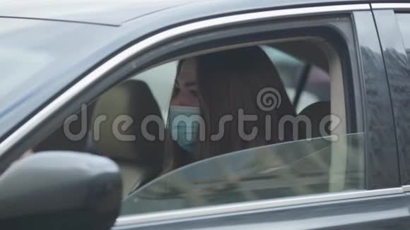 侧视肖像年轻妇女戴着保护面具坐在车里咳嗽有疾病症状的年轻妇女视频的预览图