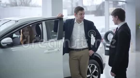 快乐的白种人年轻女人坐在车里她的丈夫和经销商交谈成功夫妇购买车辆视频的预览图