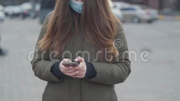 不可辨认的黑发女人戴着保护面具站在城市街道上年轻女子打电话视频的预览图