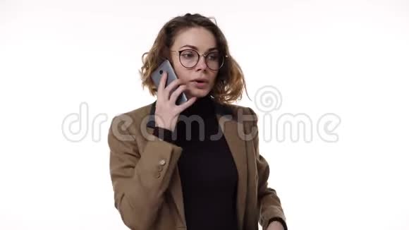 开朗的女人在讲手机兴奋的谈论白色背景在工作室戴眼镜和棕色夹克的女人视频的预览图