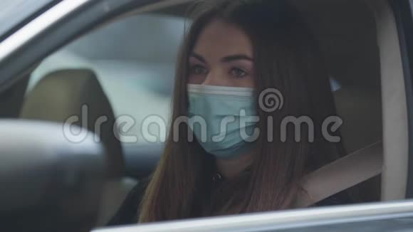 坐在驾驶座上戴防护面罩的年轻女子咳嗽特写疲惫的黑发女人与视频的预览图
