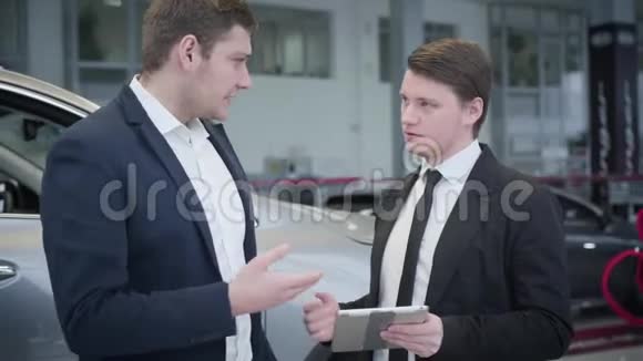 自信的白种人深色汽车经销商显示规格客户使用平板电脑销售代表讨论视频的预览图