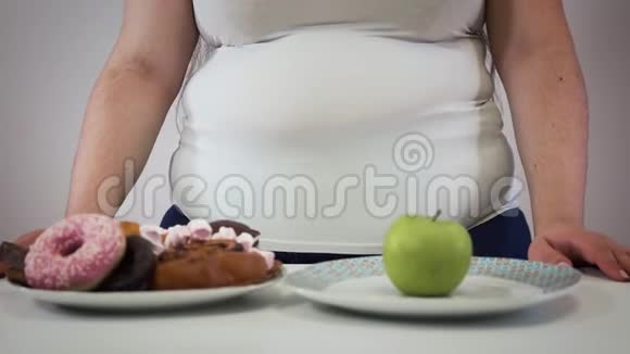 无法辨认的白种人成年女人站在桌子上桌子上放着糖果和苹果肥胖女孩选择视频的预览图