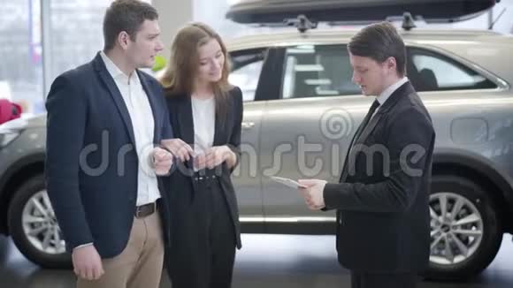 穿西装的白人和汽车经销商的年轻夫妇交谈成功的家庭在展厅买新车视频的预览图