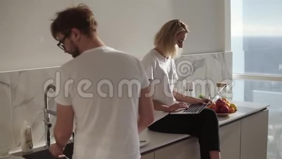 两个人一起在厨房聊天金发女人用笔记本电脑坐在厨房柜台上视频的预览图