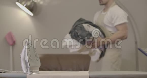 穿着围裙把衣服放在熨衣板上的白种人模糊无法辨认的男性管家做家务视频的预览图