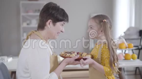 侧面看幸福的祖母和孙女拿着盘子烤着美味的煎饼擦着鼻子快乐视频的预览图