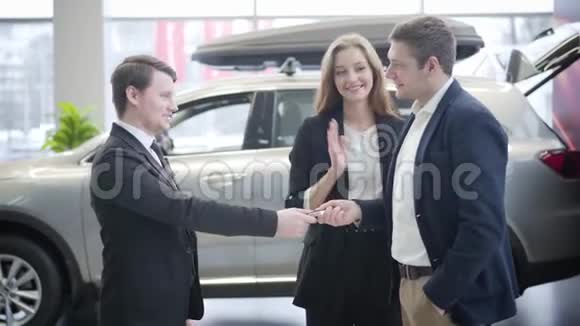 快乐的年轻白种人女人跳着拍手从丈夫那里拿着车钥匙两个男人的焦点变化视频的预览图