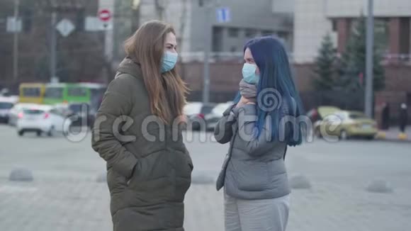 两个焦虑的女人戴着防护面具在城市街道上交谈喉咙痛朋友讨论症状视频的预览图