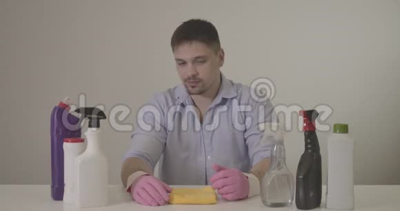 年轻男子的肖像看着站在桌子上的洗涤剂并显示拇指向下英俊的白人管家视频的预览图