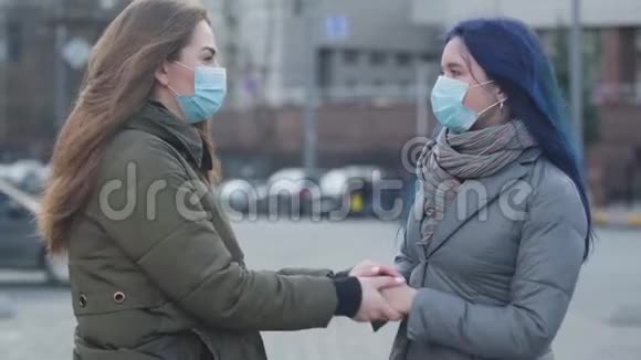 两名戴着防护面具的年轻妇女站在城市街道上交谈布鲁内特女孩和她的女朋友视频的预览图