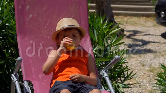 戴帽子的男孩躺在躺椅上喝橙汁视频的预览图