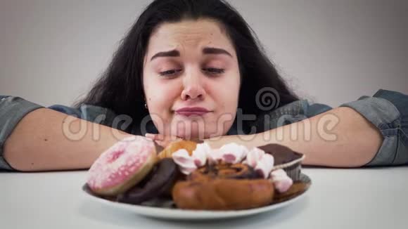 一个肤色浅黑的白人女孩端着糖果坐在盘子前饥饿的胖女人看着美味视频的预览图