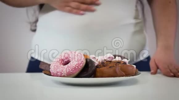 无法辨认的白种人丰满的女人抚摸着肚子盘子里放着甜点站在前台奥比斯女孩视频的预览图