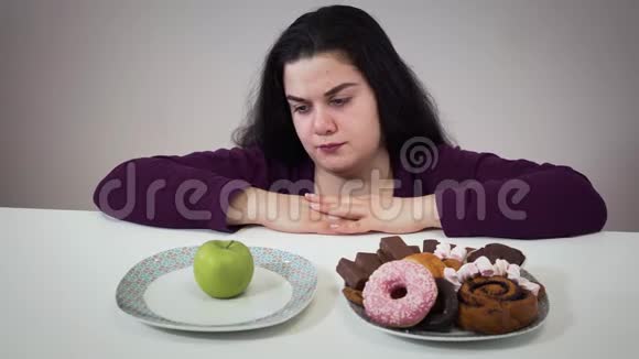 令人不安的肥胖白人妇女移动盘子与甜点和吃健康的苹果伤心的胖姑娘节食视频的预览图